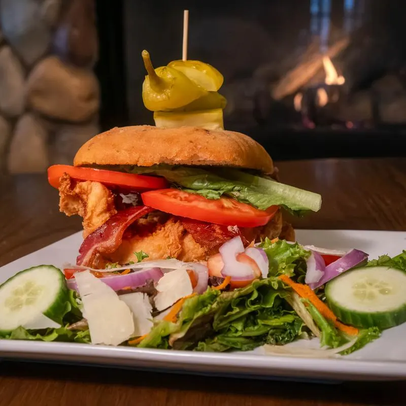 Burger with bacon and a pepper on top, served with salad.